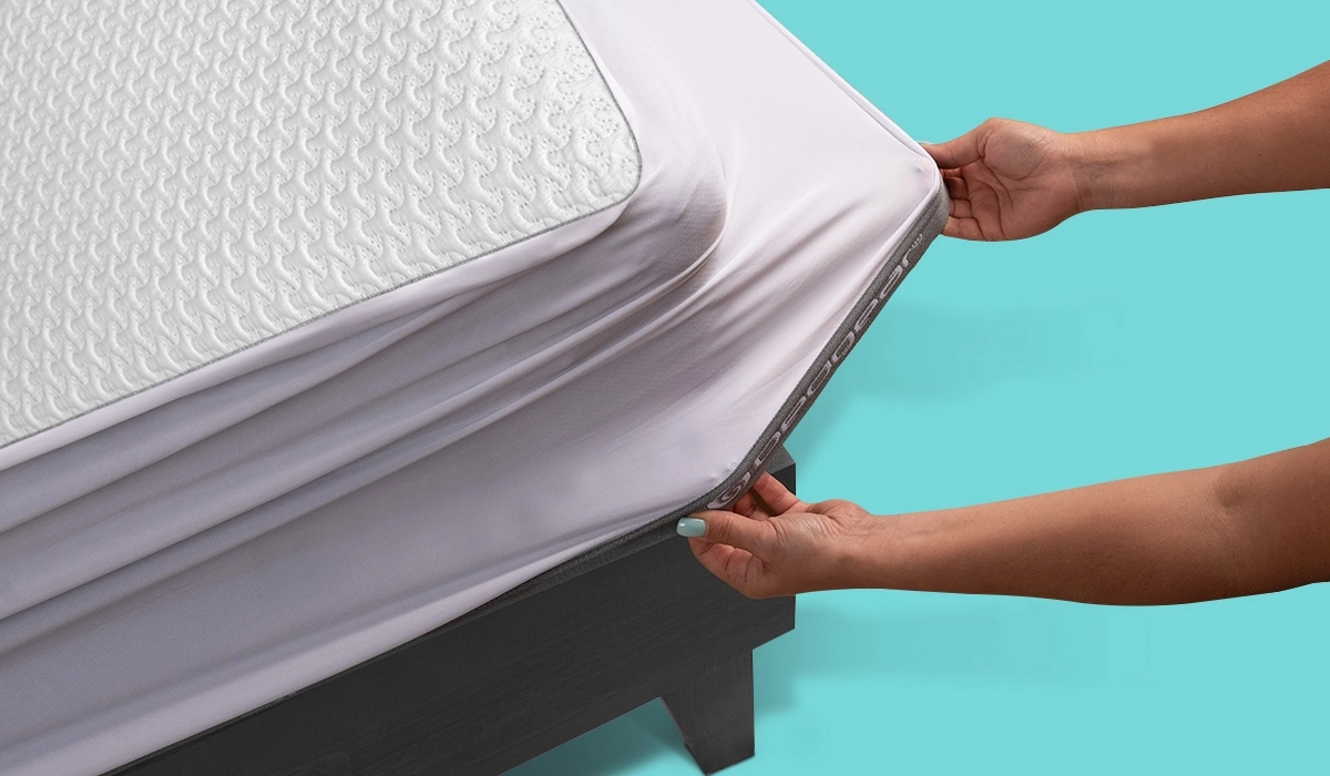 Close-up of hands adjusting a textured mattress with a white protector on a wooden frame.