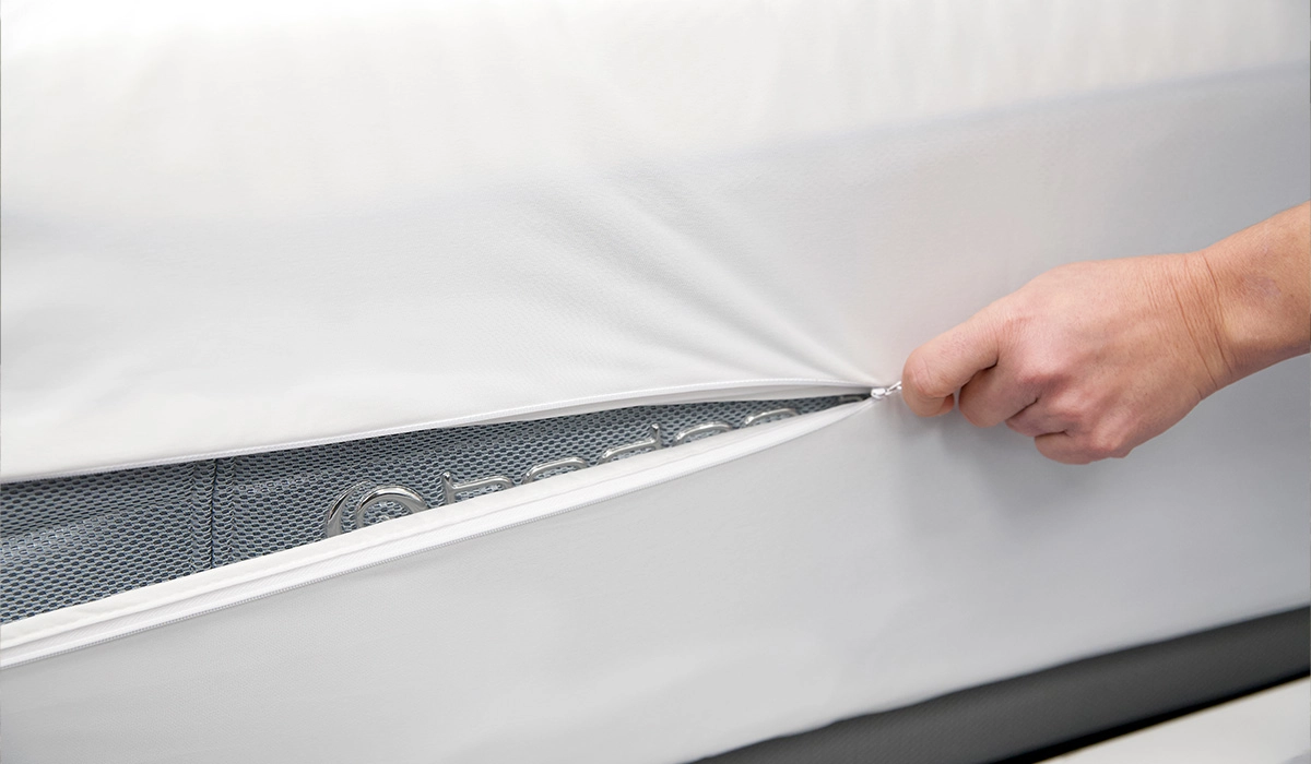 Hand reveals ventilated grid pattern on sleek white mattress cover for enhanced comfort.