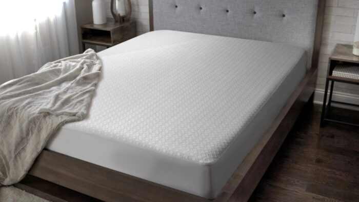 Sleek modern bedroom with white mattress, gray headboard, beige blanket, and natural lighting.