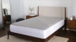 Modern wooden bed with upholstered headboard, mirrored wall, and minimalist decor.