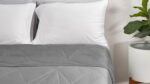 Modern minimalist bedroom with gray quilt, white pillows, and lush green plant.