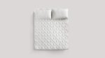 Modern white quilted bed with textured pillows in a tranquil, minimalist bedroom.