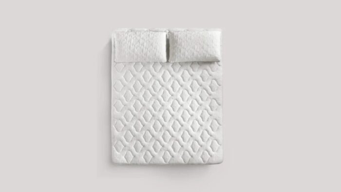 Modern white quilted bed with textured pillows in a tranquil, minimalist bedroom.