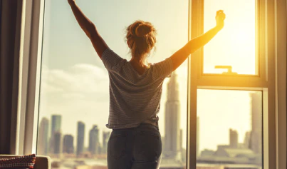 Woman stretching by window overlooking city skyline at sunrise, embracing tranquility amidst urban energy.