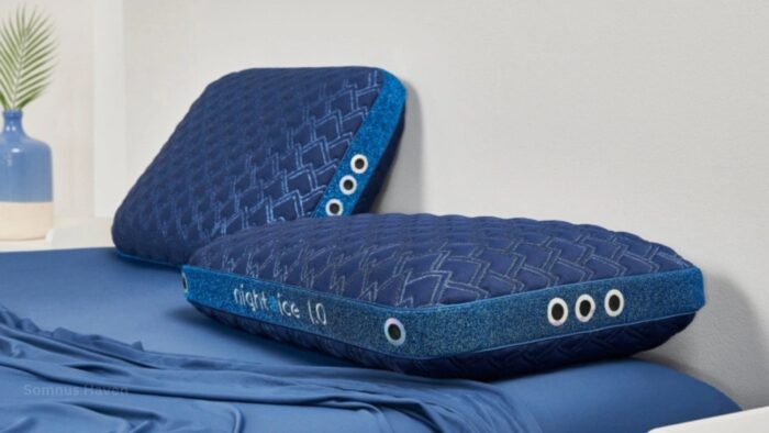 Navy pillows with eye-like details on a neat bed with a green leaf vase nearby.