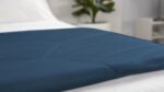 Elegant navy quilted blanket on white bedding with green plant for a tranquil, minimalistic room.