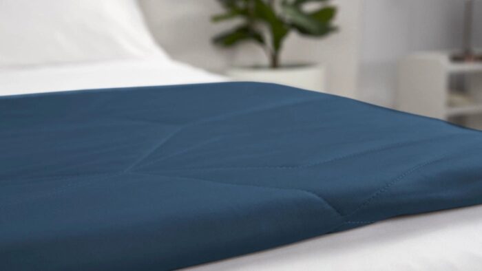 Elegant navy quilted blanket on white bedding with green plant for a tranquil, minimalistic room.