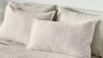 Neutral bedding with chevron pillows creates a tranquil, sophisticated bedroom atmosphere.