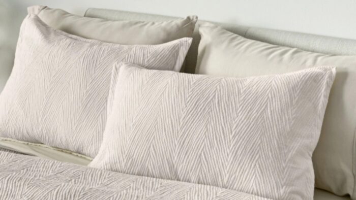 Neutral bedding with chevron pillows creates a tranquil, sophisticated bedroom atmosphere.