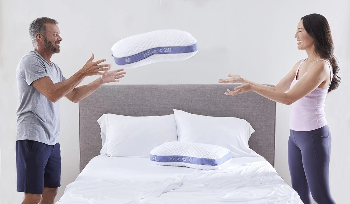 Joyful couple enjoys playful pillow fight on a stylish bed with quality bedding.