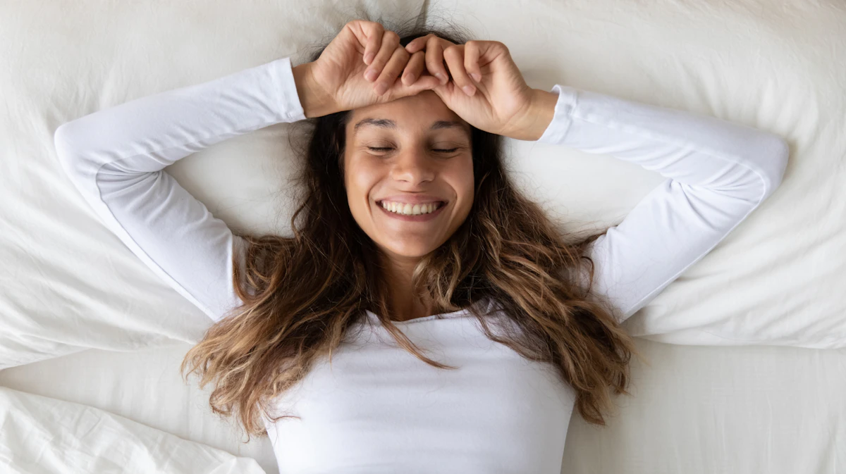 Young woman smiling in serene comfort on a fluffy white bed.