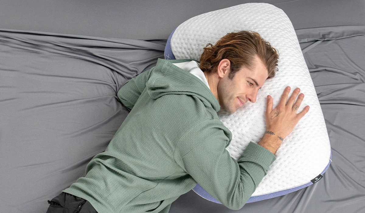 Man relaxing with ergonomic pillow on minimalist gray bed linens for restful sleep.