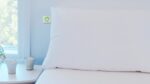Minimalist bedroom with white pillow, ribbed vases, and soft blue walls.