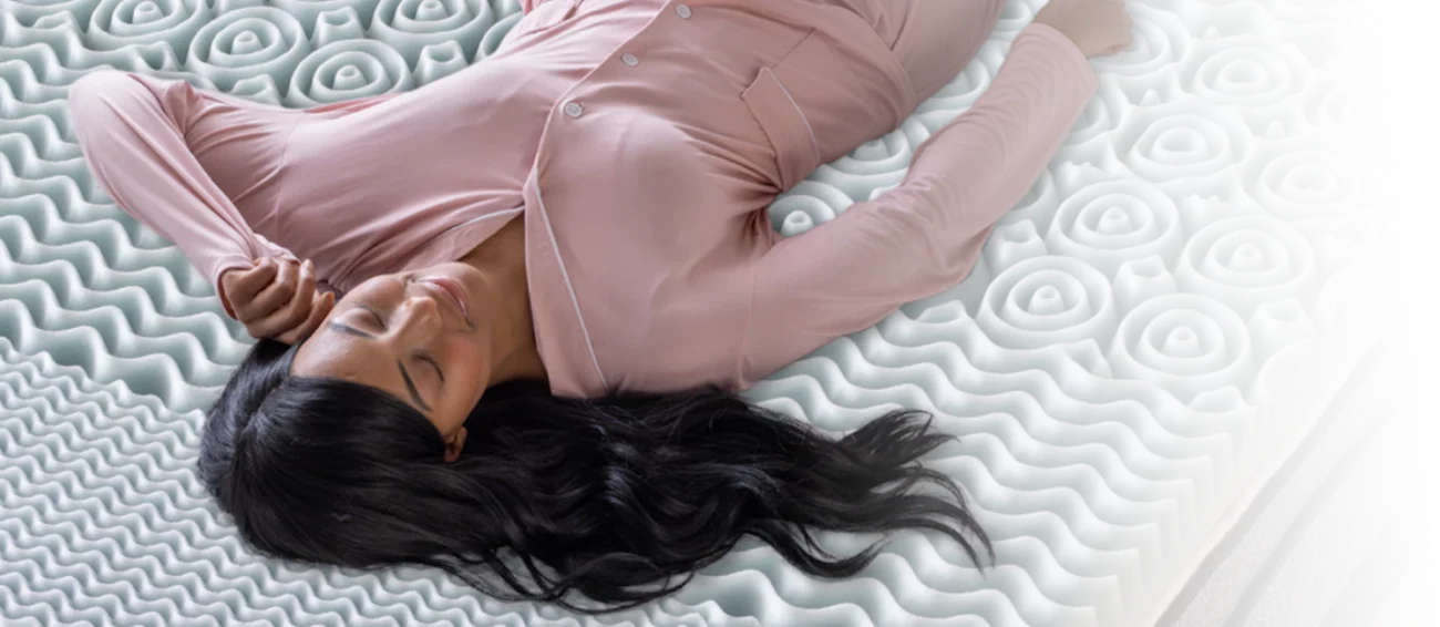 Woman in pink pajamas relaxing on a uniquely designed, ergonomic mattress for restful sleep.
