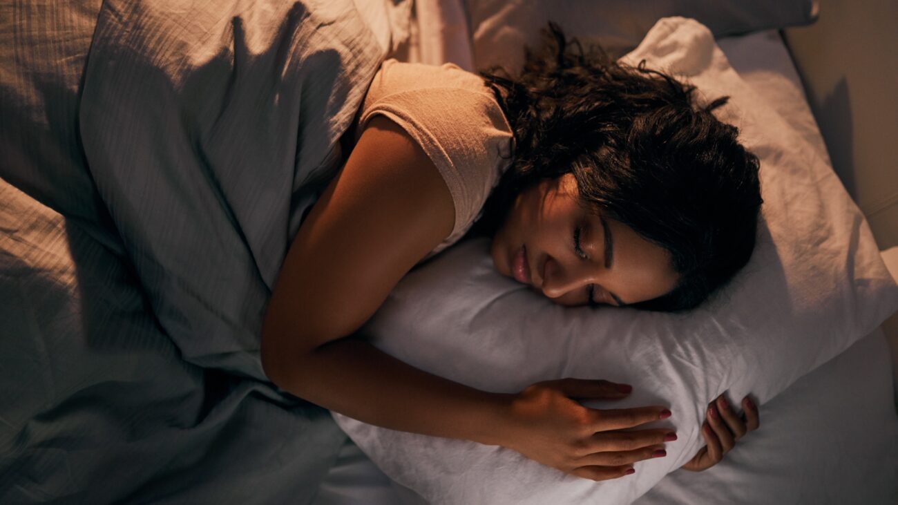 A woman peacefully asleep in a cozy, softly-lit bedroom with light bedding.