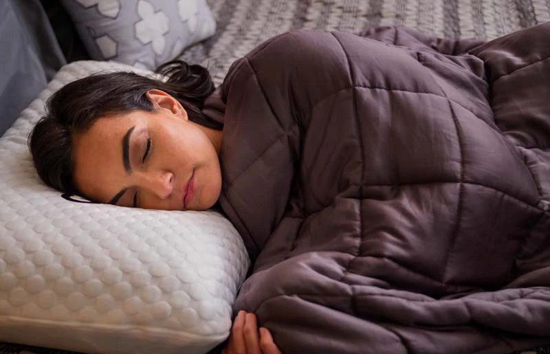 Woman peacefully sleeping in cozy room with quilted blanket and plush pillows.