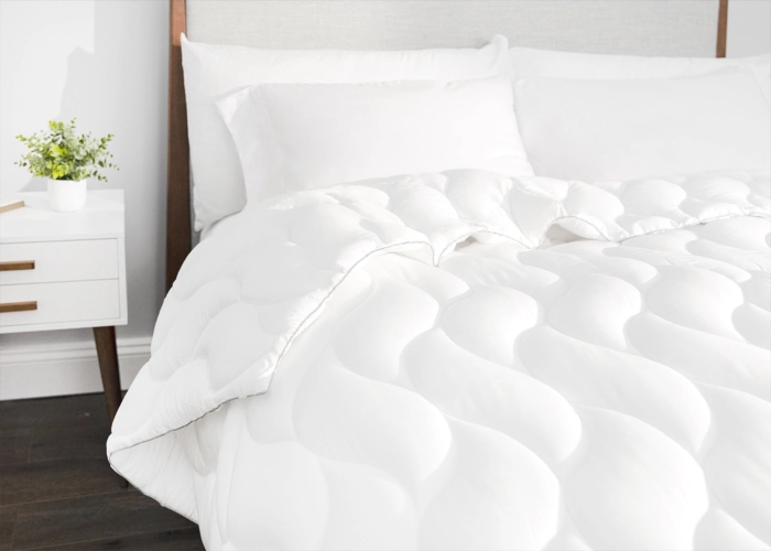 Serene bedroom with white quilted bedding, minimalist nightstand, potted plant, and dark wood floor.
