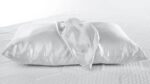 White satin pillow with silk scarf detail on textured bed.