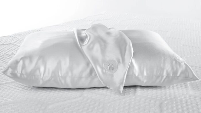White satin pillow with silk scarf detail on textured bed.