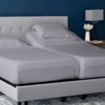 Modern bedroom with a split king bed, gray headboard, blue wall, and wooden nightstands.