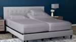 Modern bedroom with a split king bed, gray headboard, blue wall, and wooden nightstands.