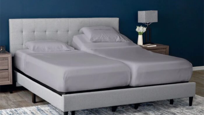 Modern bedroom with a split king bed, gray headboard, blue wall, and wooden nightstands.