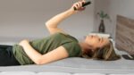 Woman relaxing on a mattress, using smartphone in serene modern bedroom.
