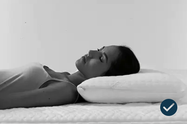 Tranquil woman resting on soft bedding with supportive pillow in monochrome setting.